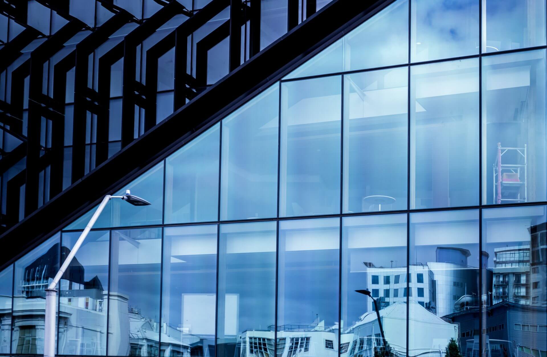 An angular glass-clad building reflecting the street and sky at dusk