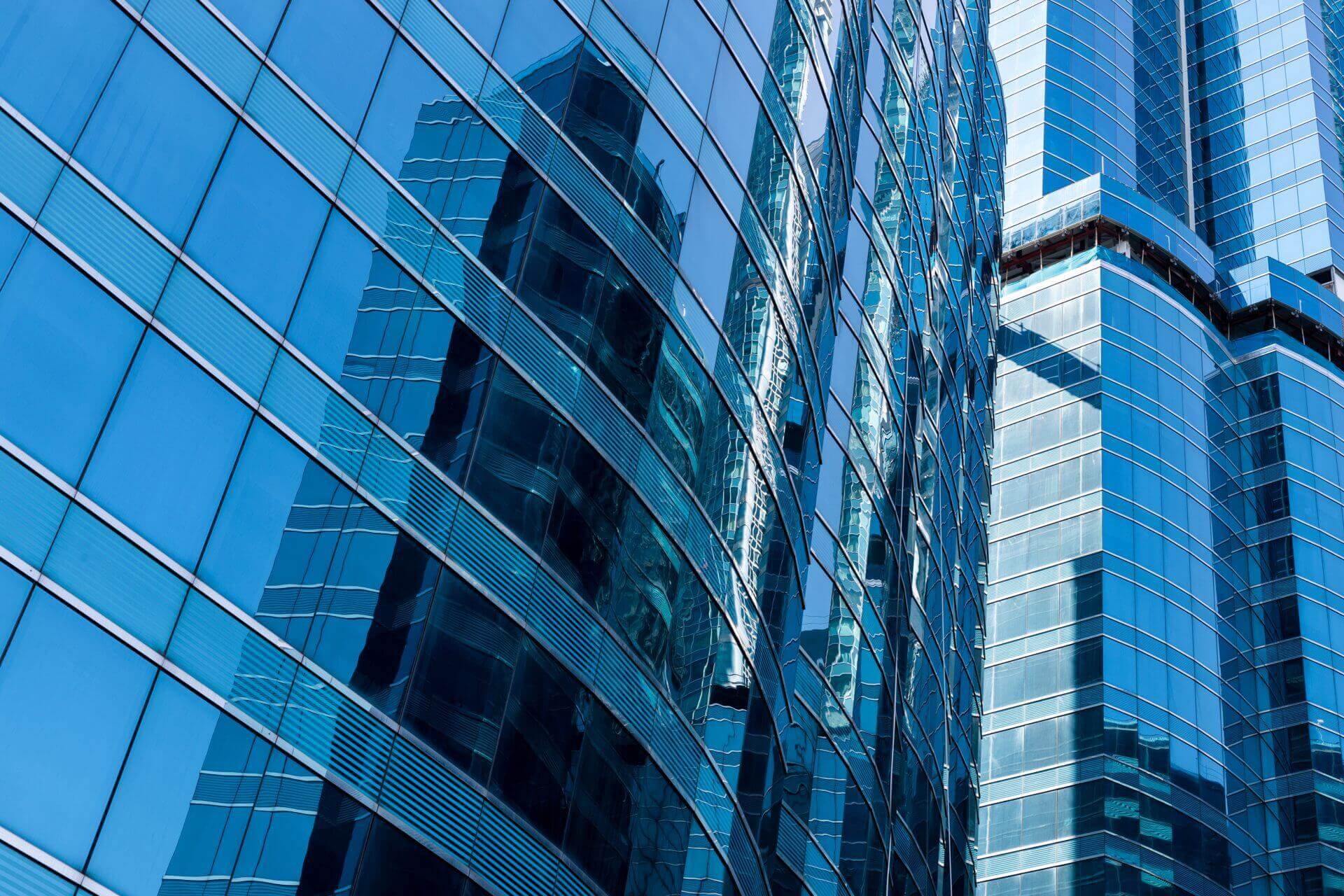 A blue glass curtain wall on a high-rise, its neighbours reflected in the glazing