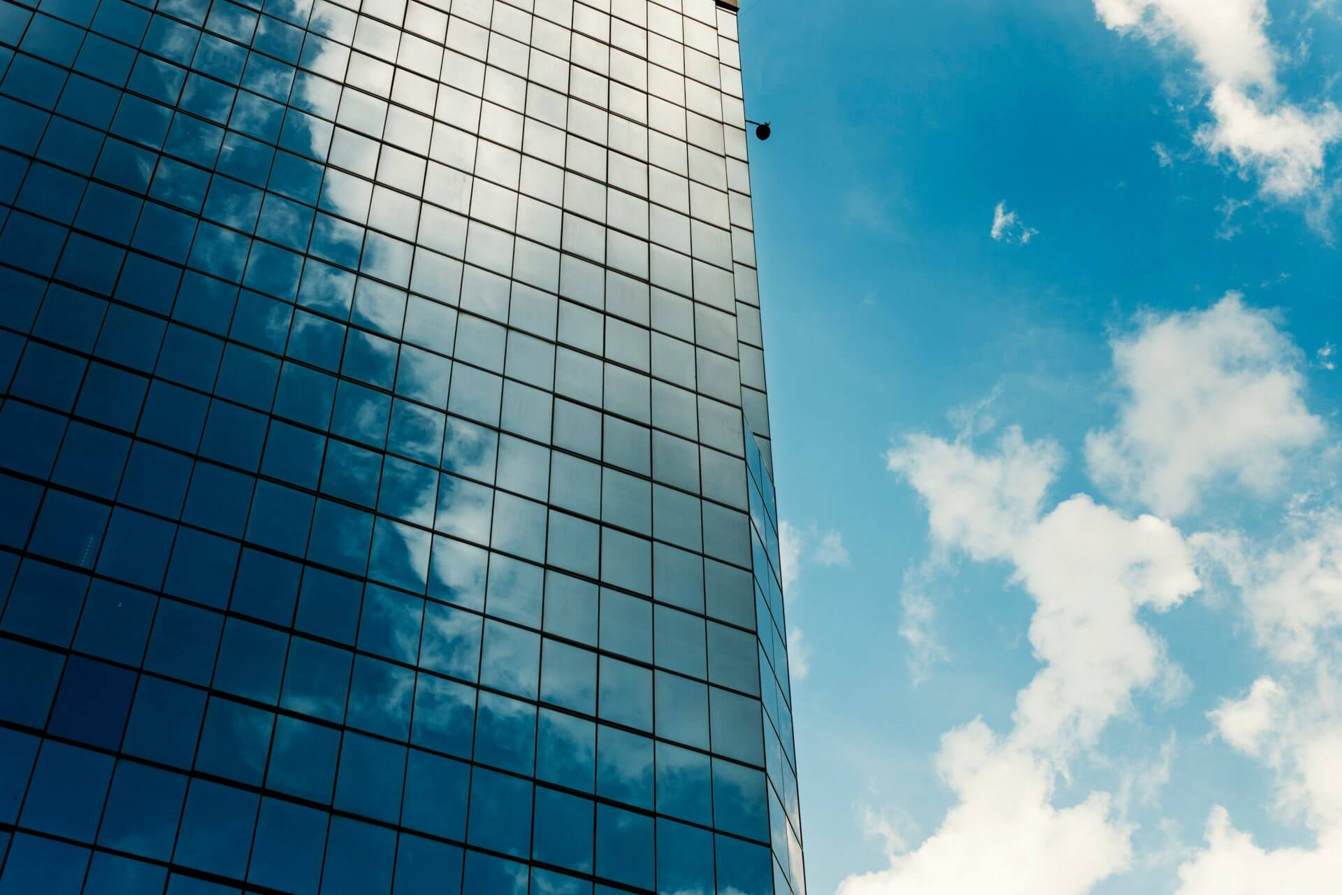 Gridded glass curtain wall reflecting cloud against a blue sky