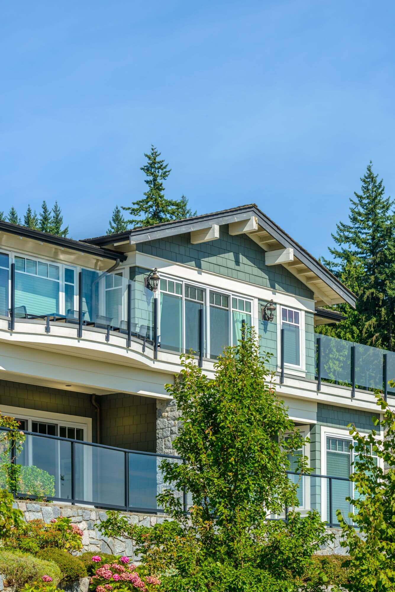The upper storey of a coastal home with picture windows and a glass balcony rail
