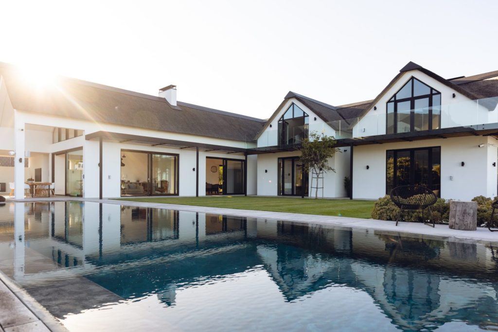 A modern white house with full-height sliding glass doors reflected in a pool