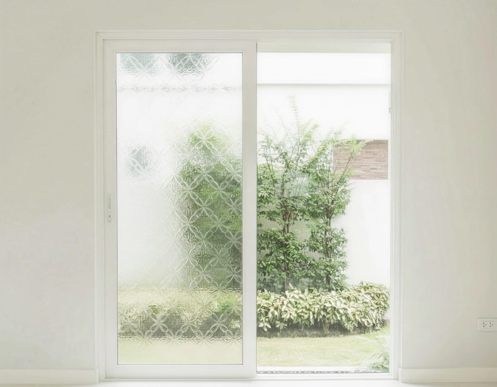 A patio door whose left panel is decorative patterned glass, with a garden beyond the clear leaf